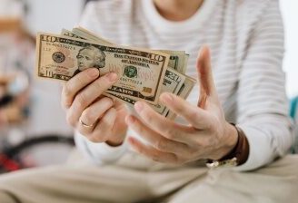 Close-up of a person sitting on a bed holding a large spread of US dollars