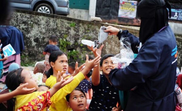 A group of children clamor for items being handed out by an adult.